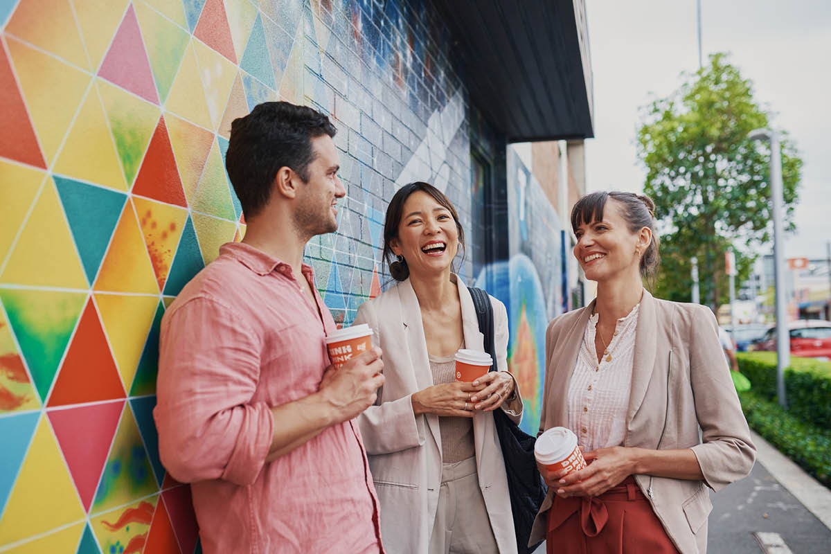 Young corporate workers drinking coffee and talking in front of a mural wall